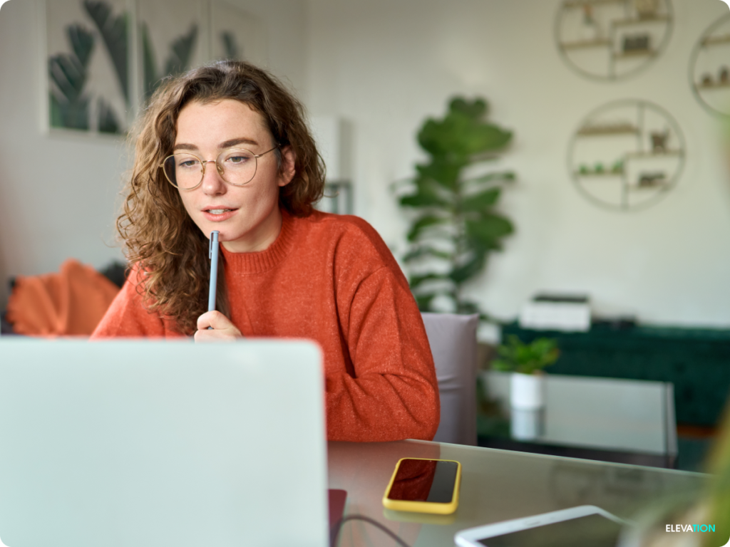Elevation Young female sitting at a laptop computer holding pen