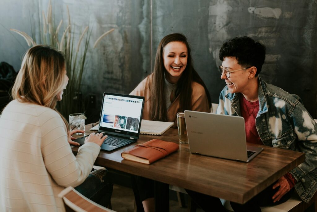 Three nonprofit teammates laughing together around a table with laptops