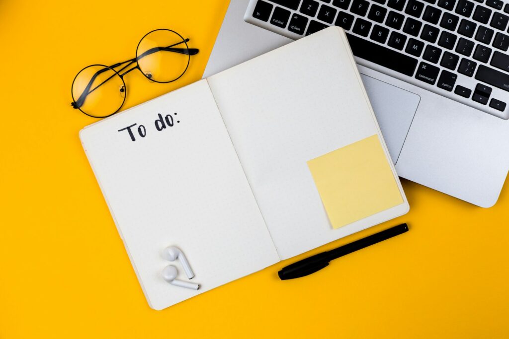 Notebook laptop and glasses laid out on a yellow desk
